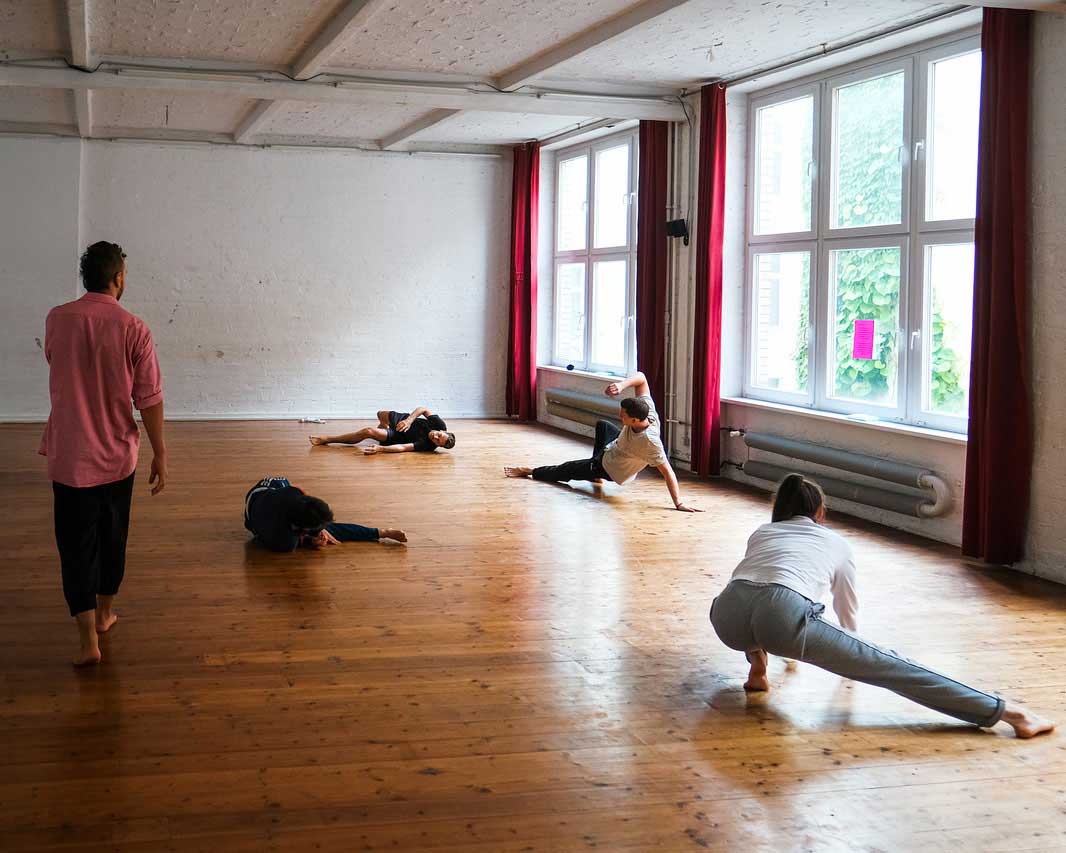 Luis Stängl bei einem seiner Kurse im Tanzstudio. Luis kontrolliert die Dehnübungen von 4 Schülerinnen und Schülern auf dem Boden.
